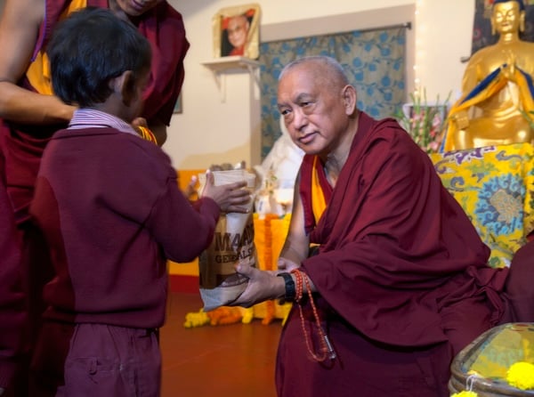 Lama Zopa Rinpoche offering food to a young student at Maitreya School in Bodhgaya, India